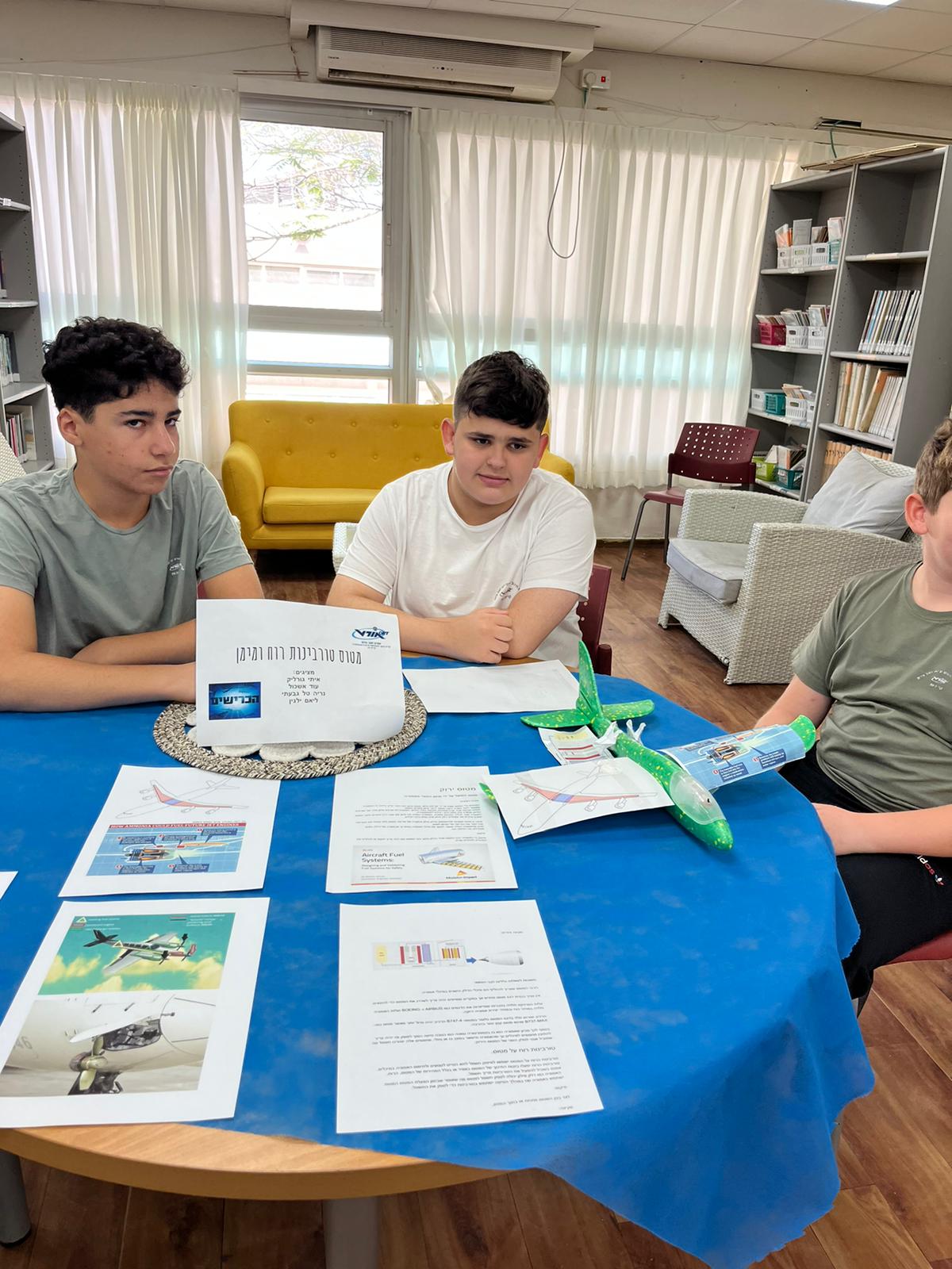 תלמידים יושבים בקבוצה סביב שולחן, דגם מטוס על השולחן
